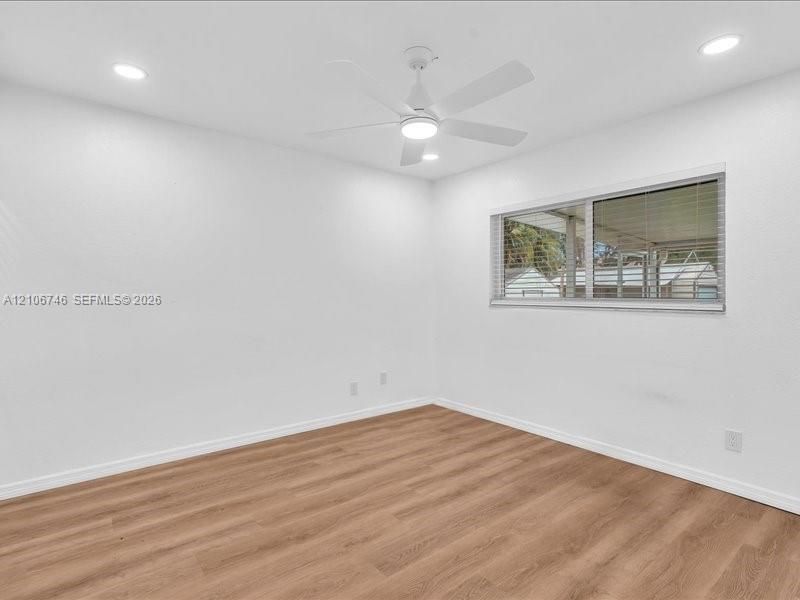 Interior space featuring wood-finish flooring, white walls, recessed ceiling lighting, and a white ceiling fan with integrated lighting