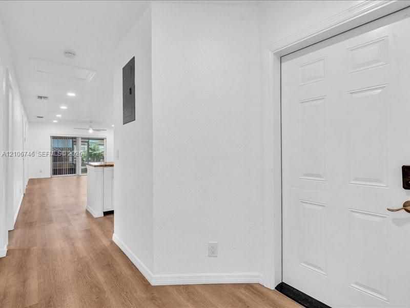 Six-panel interior door with brushed metal hardware, wood-finish flooring, recessed ceiling lighting, and a white interior palette