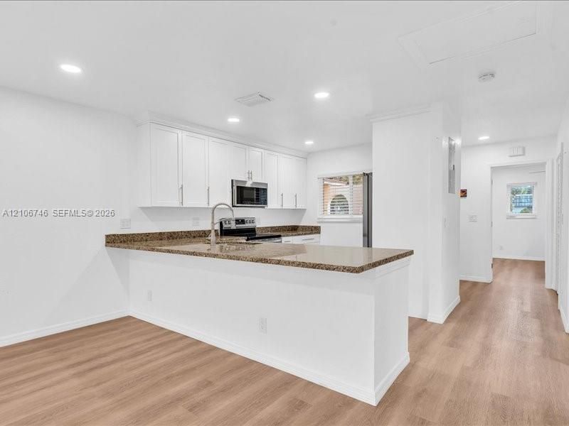 Kitchen featuring white cabinetry, stone-surface countertops, wood-finish flooring, recessed lighting, and a stainless steel over-the-range microwave