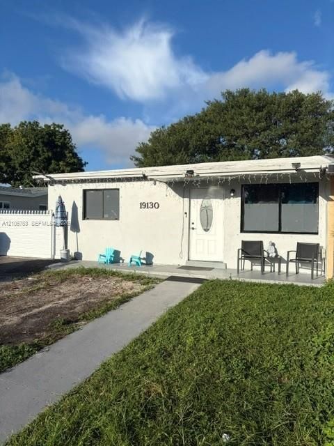 Single-story exterior featuring light-toned stucco siding, a central entry door with oval glass insert, horizontal sliding windows, and a white privacy fence
