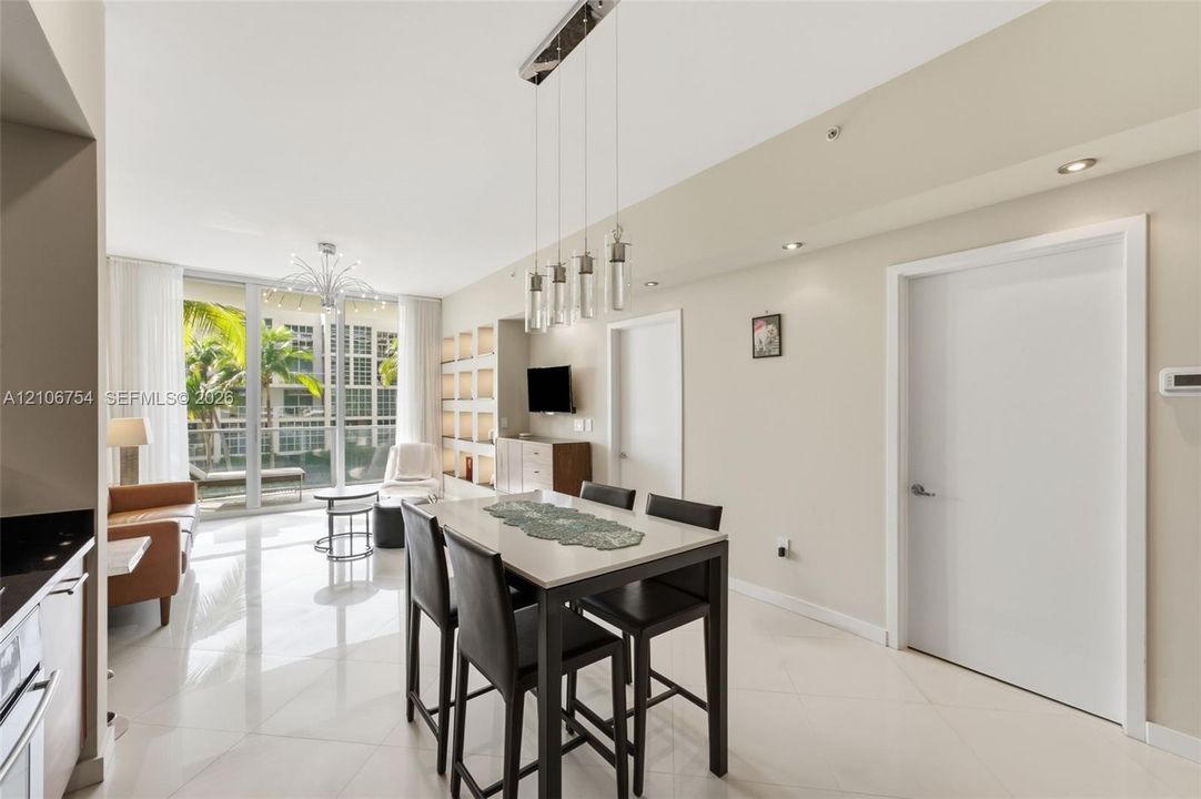 Open-concept living space featuring floor-to-ceiling glass windows, recessed ceiling lighting, a multi-pendant light fixture, and built-in wall shelving