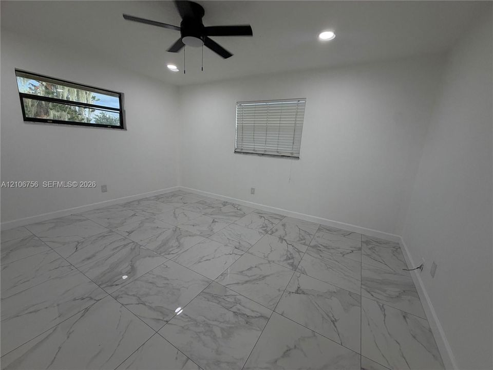 Large-format tile flooring, recessed ceiling lighting, and a modern ceiling fan, punctuated by two windows featuring horizontal blinds