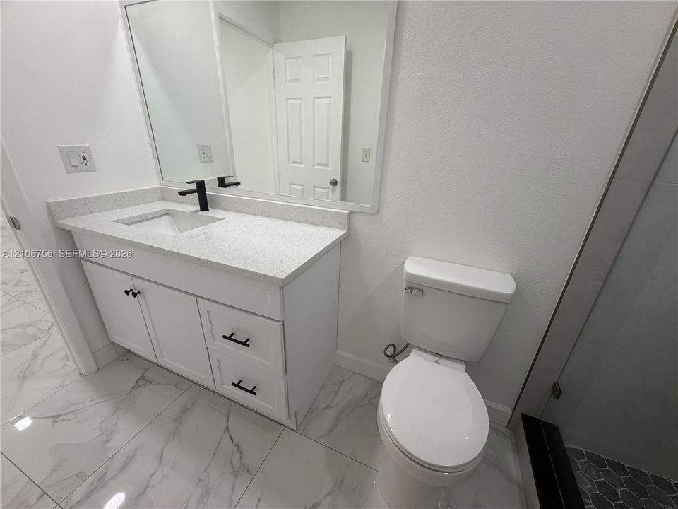 White vanity cabinet featuring a solid-surface countertop with an integrated basin, matte black hardware, a wall-to-wall mirror, and large-format porcelain tile flooring