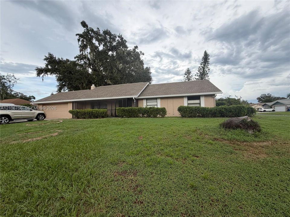 Single-story residence featuring a shingled roof, attached two-car garage, covered screen-enclosed front porch, and mature landscaping