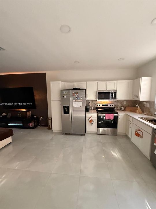 Kitchen featuring white cabinetry, stainless steel appliances, and large-format tile flooring, complemented by recessed lighting and an accent wall