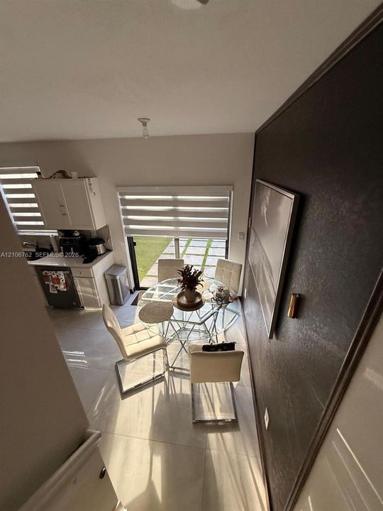 Large-format tile flooring, textured accent wall, sliding glass door, roller shade window treatments, and white cabinetry
