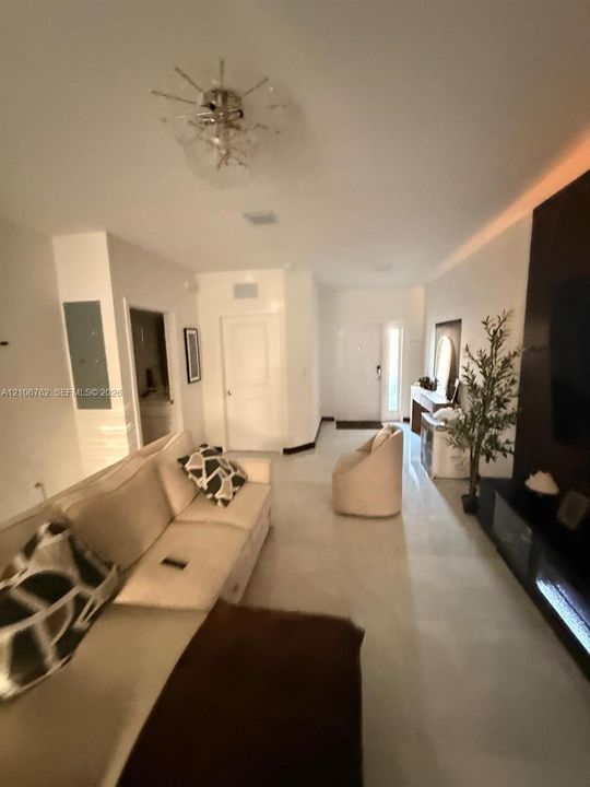 Living area featuring polished tile flooring, a dark built-in entertainment console with integrated lighting, recessed tray ceiling accent, and a modern sputnik-style flush mount light fixture