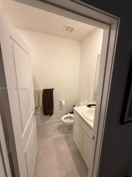 Bathroom featuring light-toned tile flooring, a white vanity cabinet, a solid-surface countertop with an integrated sink, and chrome fixtures