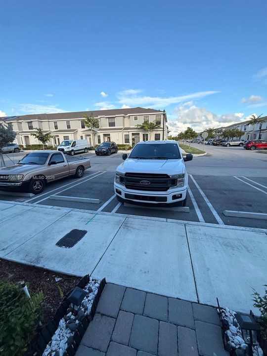 Exterior concrete walkway with stone-paver border and designated paved parking area
