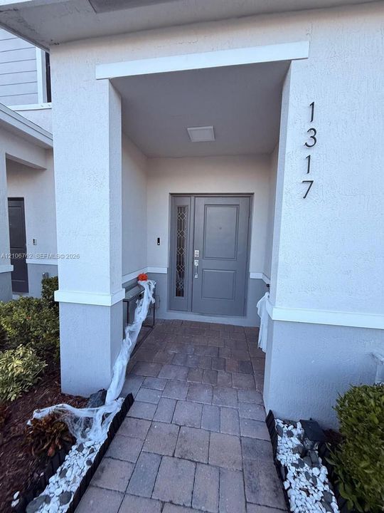 Covered entryway featuring stone paver flooring, a gray front door with decorative glass sidelight, and vertical address numerals