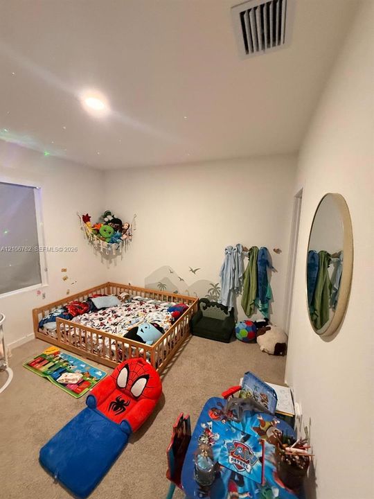 Neutral-toned room featuring wall-to-wall carpeting, a large rectangular window, and a circular wall-mounted mirror