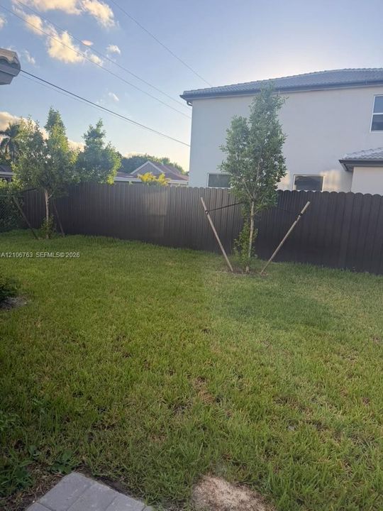 Private backyard featuring a fenced perimeter, grass lawn, and young trees