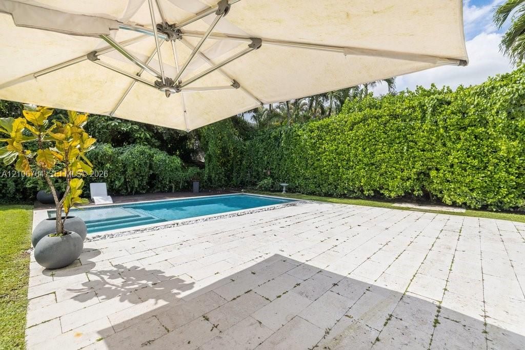 Outdoor living area featuring a light-toned stone patio, a rectangular swimming pool with a built-in step, and perimeter landscaping consisting of mature privacy hedges