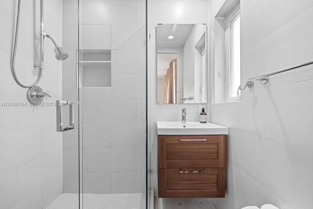 Bathroom featuring a wood-finish vanity with a rectangular sink, wall-mounted mirror, glass-enclosed shower with a built-in recessed niche, and polished metal fixtures