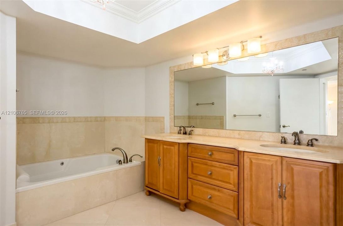 Main bathroom, soaking tub with stone tile surround, dual-sink vanity with wood cabinetry, and large wall-mounted mirror