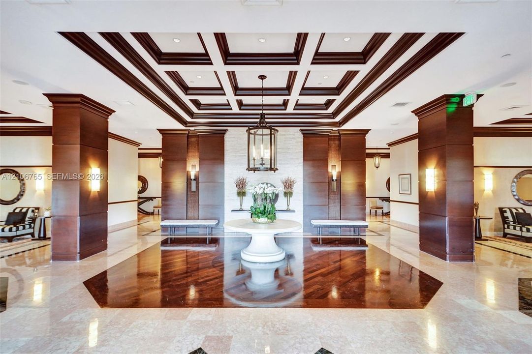 Grand entrance hall, offered ceiling with wood detailing, natural stone flooring with a dark wood-finish inlay, large wood-panelled columns, custom hanging lantern lighting, and a stacked stone accent wall.