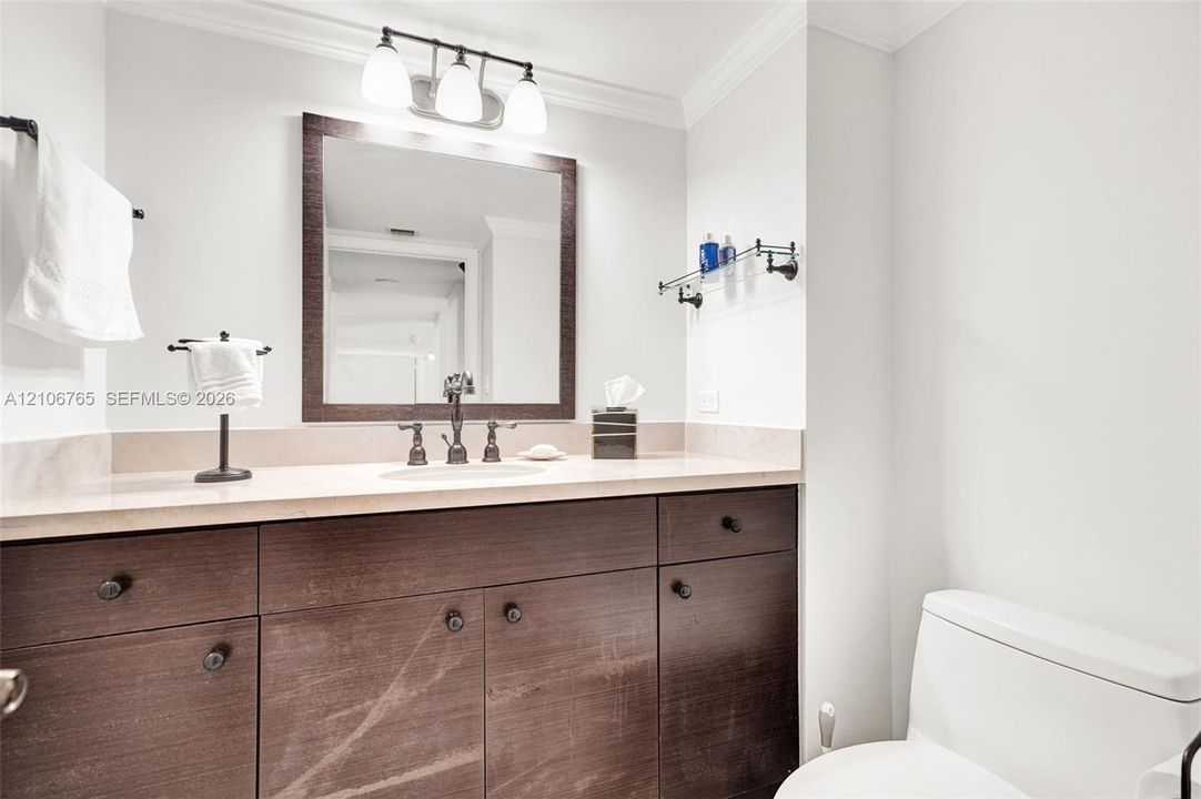 Second bathroom, dark wood-finish cabinetry, light-toned stone countertop, integrated undermount sink,  oil-rubbed bronze faucet, three-light vanity fixture, and rectangular framed mirror.