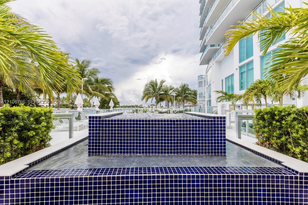 Outdoor water feature clad in cobalt blue tile, surrounded by manicured landscaping, palm trees, and structural glass balustrades