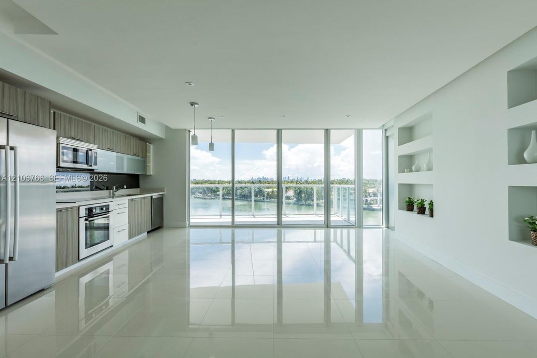 Contemporary kitchen featuring stainless steel appliances, wood-finish cabinetry, floor-to-ceiling glass paneling, polished tile flooring, and recessed wall shelving