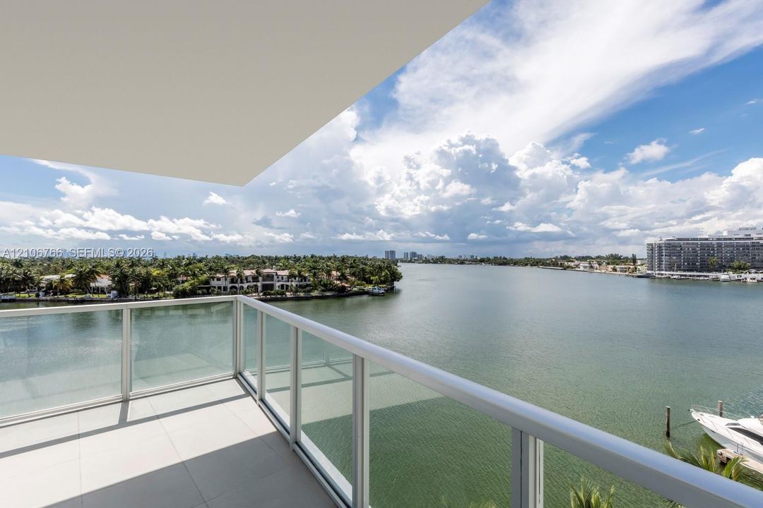 Private balcony featuring large-format tile flooring and a glass-paneled metal railing overlooking the waterfront