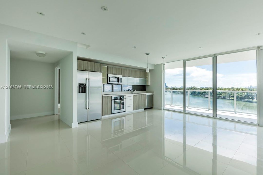 Open-concept interior featuring light-toned tile flooring, recessed ceiling lighting, stainless steel appliances, horizontally-grained cabinetry, and floor-to-ceiling glass panel doors