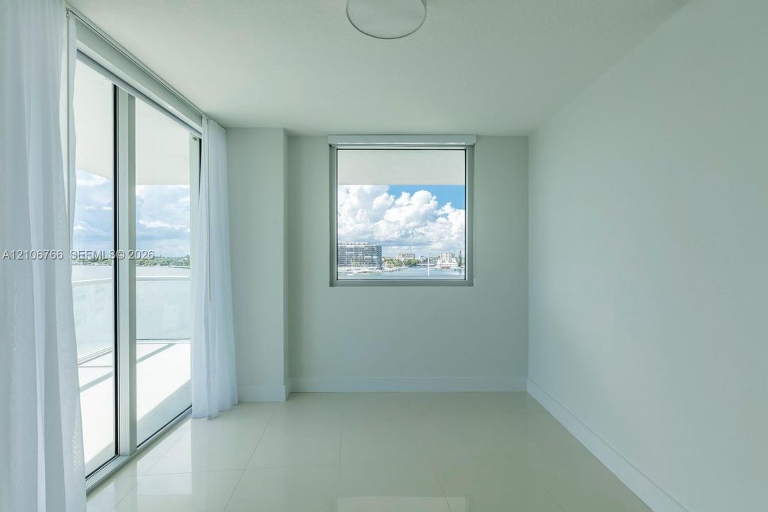 Floor-to-ceiling sliding glass doors, polished tile flooring, neutral wall finish, and energy-efficient windows with water scenery