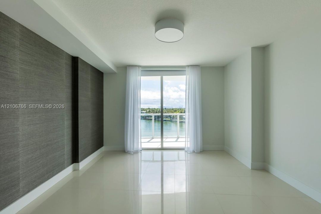 Interior space featuring large-format tile flooring, textured charcoal accent wall, flush-mount ceiling lighting, and sliding glass doors leading to a balcony