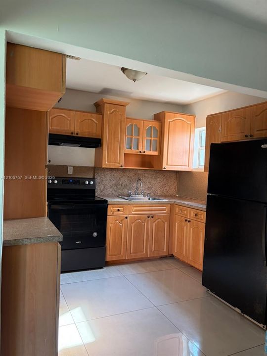 Kitchen featuring wood-finish cabinetry with glass-front accents, solid-surface countertops, tile flooring, and integrated black appliances