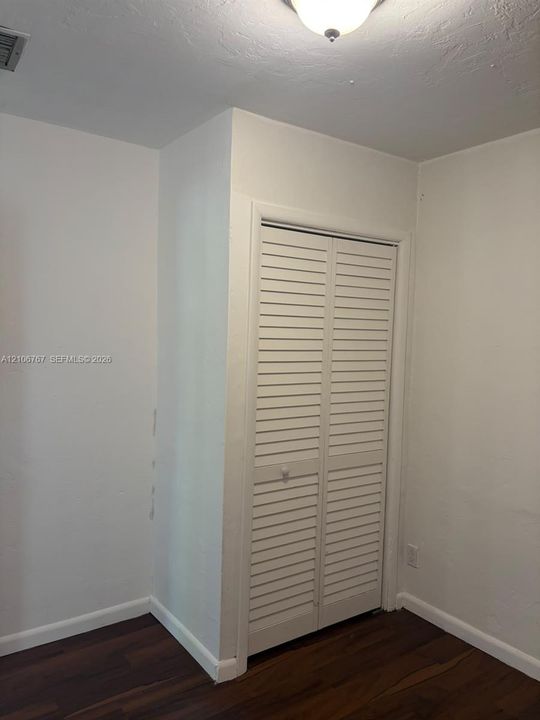 Closet featuring white louvered bifold doors, dark wood-finish flooring, and a flush-mount overhead light fixture