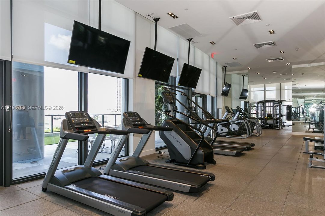 Fitness center featuring floor-to-ceiling windows, recessed lighting, tile flooring, and wall-mounted televisions