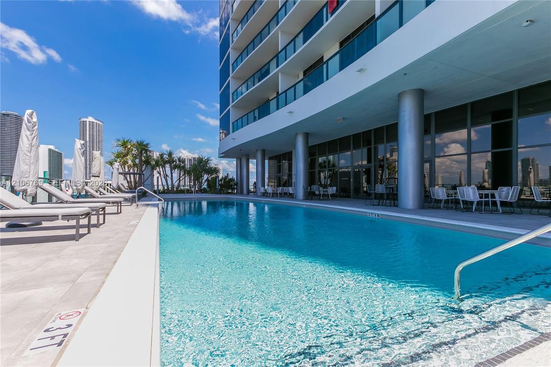 Outdoor swimming pool featuring a concrete deck, glass balcony railings, structural pillars, and floor-to-ceiling windows