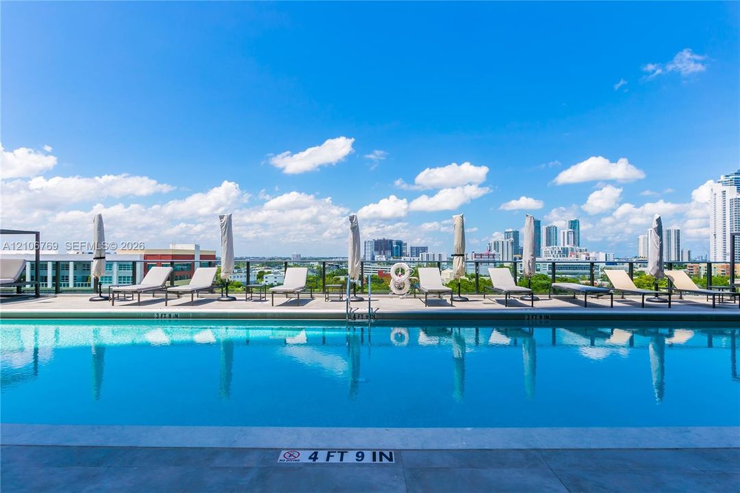 Rooftop swimming pool featuring stone-style decking, a metal perimeter railing, and an urban skyline backdrop