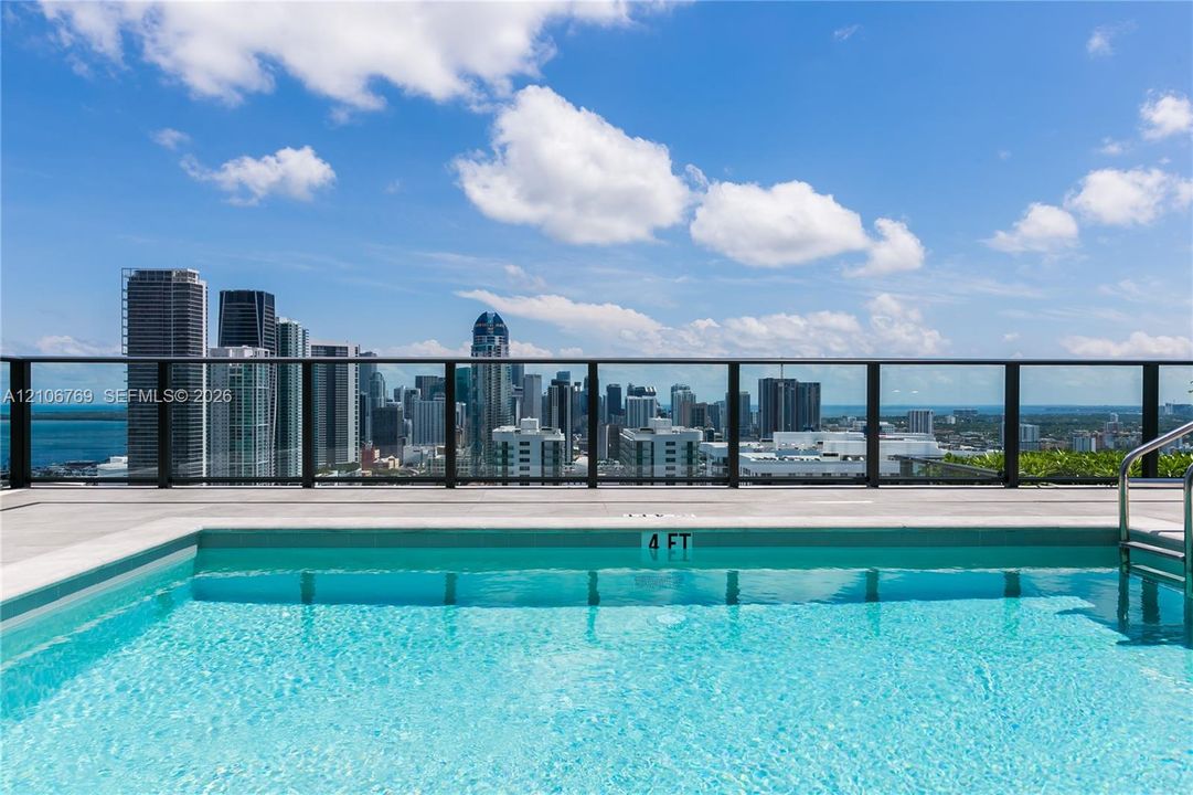 Rooftop swimming pool featuring a concrete deck and black metal railing