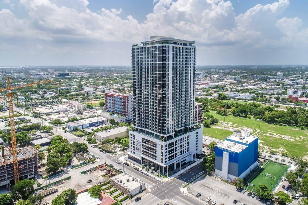 High-rise tower featuring a glass facade, recessed balconies, a multi-level parking podium, and a rooftop amenity deck