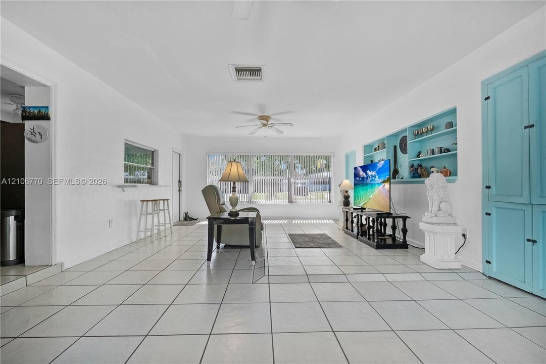 Living area featuring large-format ceramic tile flooring, built-in recessed shelving, integrated storage cabinetry, and a ceiling fan