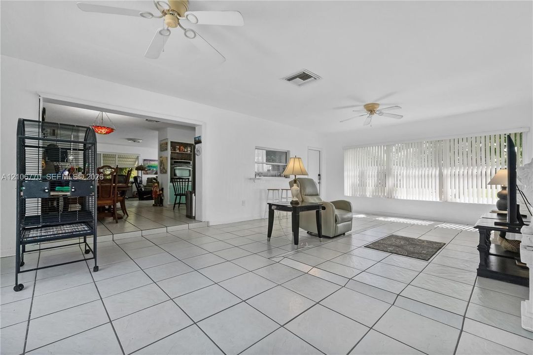 Living area featuring white ceramic tile flooring, dual ceiling fans, and large windows with vertical blinds
