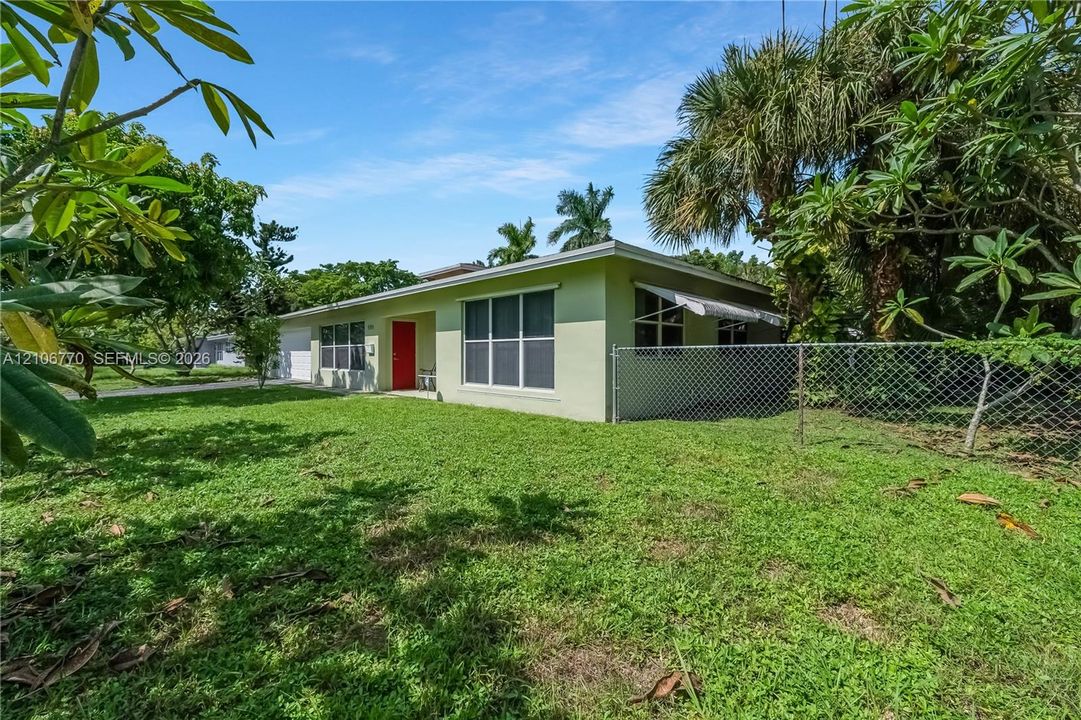 Single-story residence featuring light-colored stucco siding, a bold red entry door, large grid-pattern windows, and a chain-link fenced perimeter