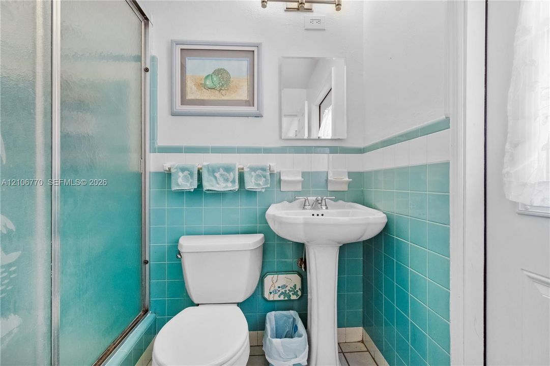 Bathroom featuring teal wall tiling with white accent trim, a white pedestal sink, a glass-enclosed shower, and built-in ceramic soap dishes