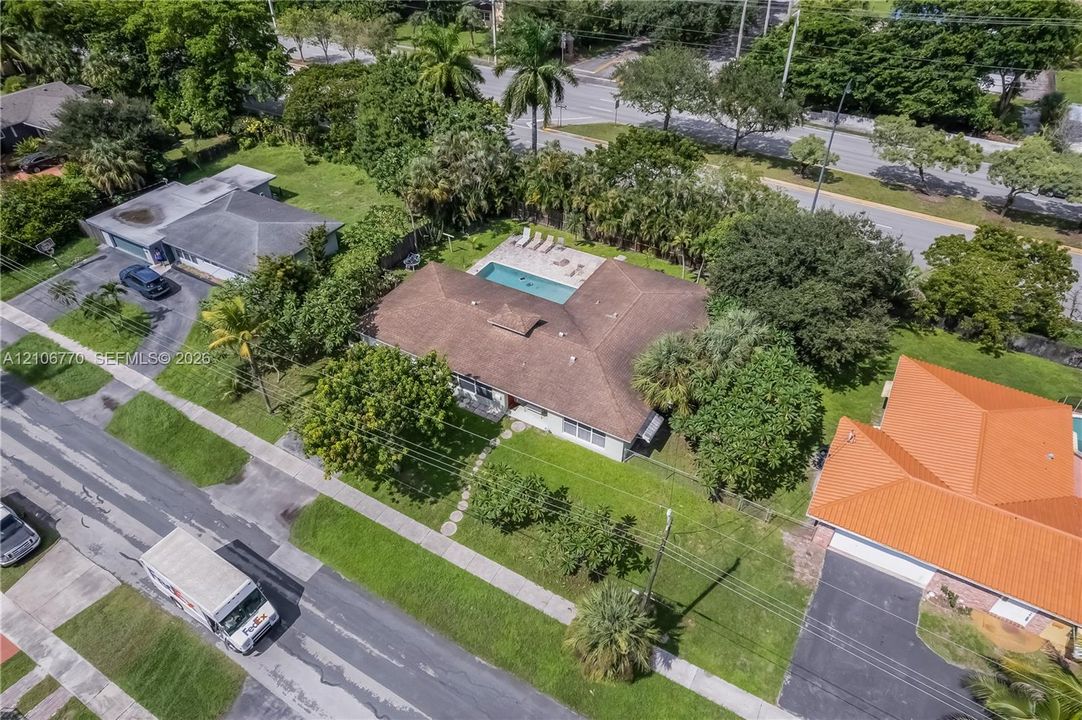 Aerial view of residential property featuring a hip-roof structure, in-ground swimming pool, stone-paver patio, and mature landscaping