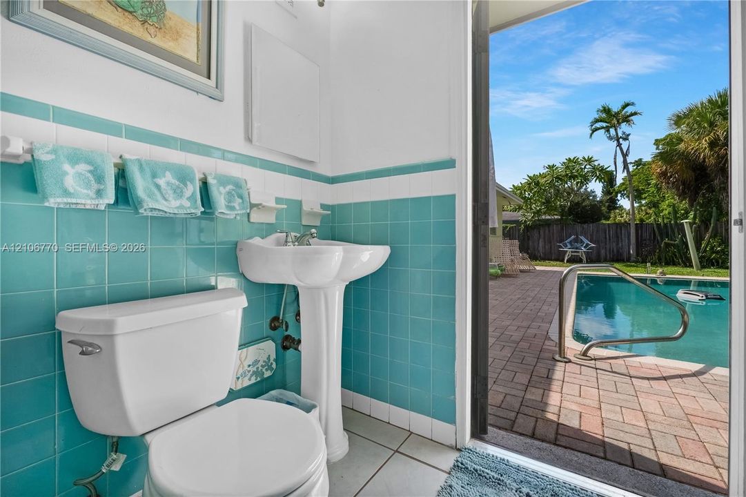 Ceramic tile wainscoting, white porcelain pedestal sink, and direct egress to a brick-paved pool deck