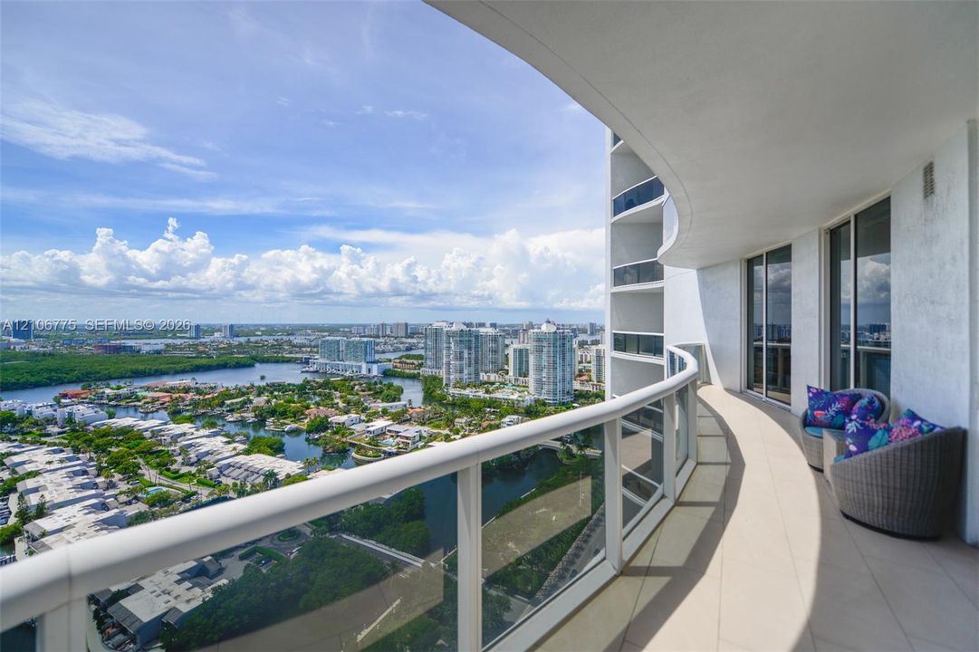 Curved private balcony featuring large-format tile flooring and a glass-panel railing with a top rail