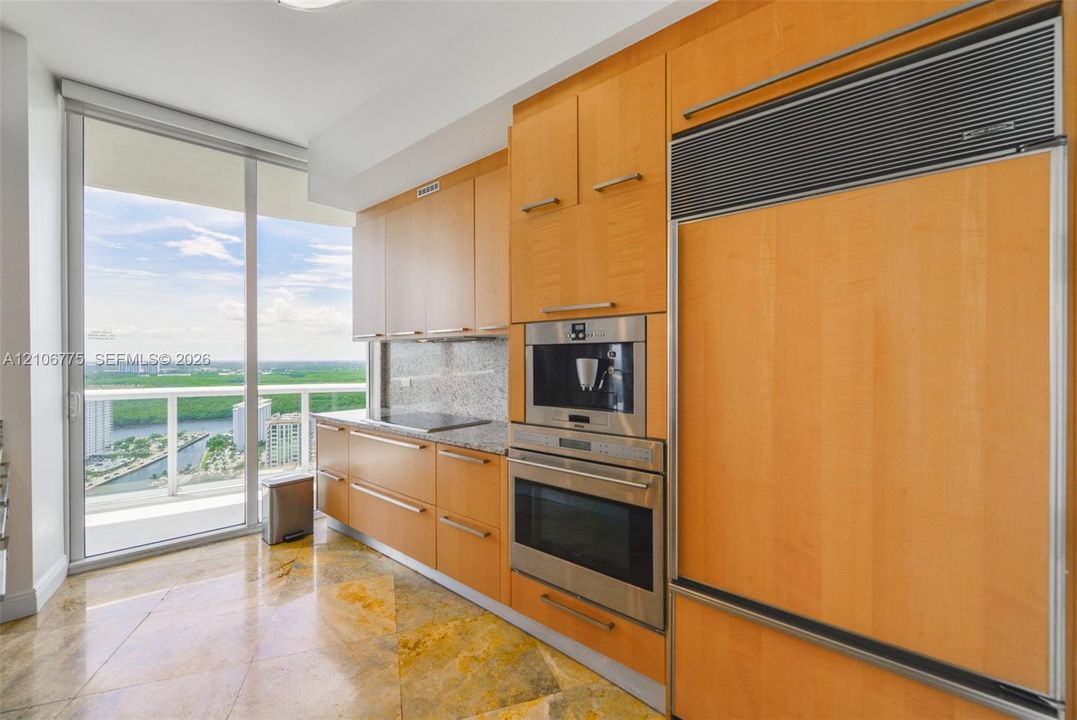 Kitchen featuring wood cabinetry, stone countertops, stainless steel built-in oven and espresso machine, panel-ready refrigerator, and stone tile flooring