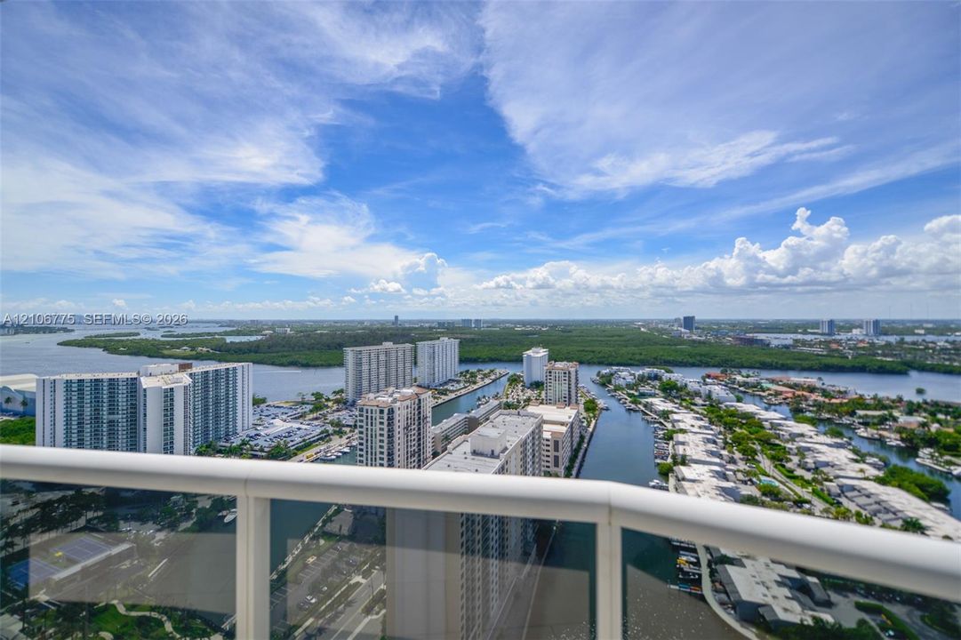 Elevated balcony featuring a glass panel railing and panoramic vistas of the surrounding waterway, coastal foliage, and urban skyline