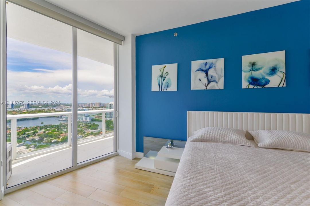 Floor-to-ceiling glass sliding doors opening to a private balcony, wood-finish flooring, and an expansive cityscape backdrop