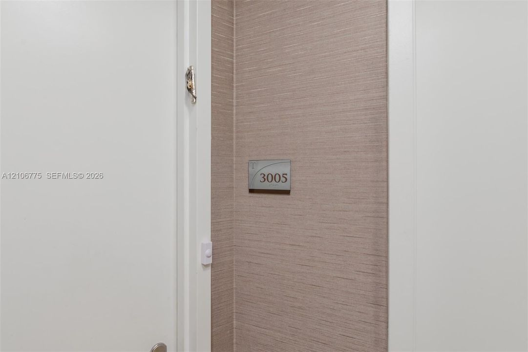 Textured wall covering in a neutral finish with a brushed metal unit identification plaque and white door trim