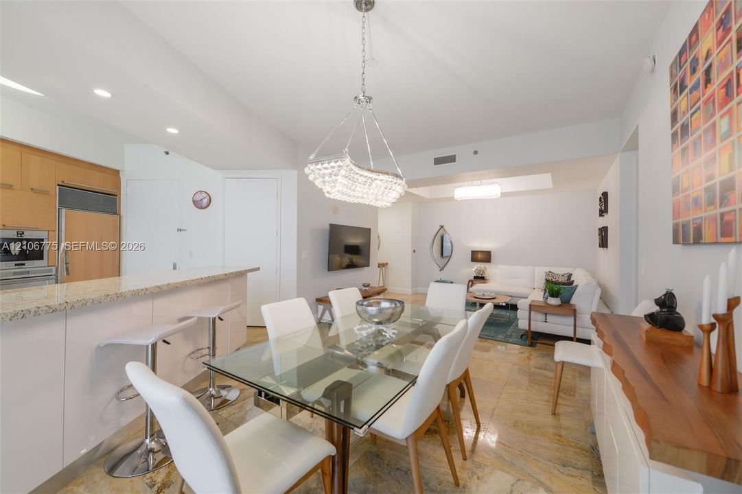 Kitchen featuring stone countertops, integrated stainless steel appliances, and wood-finish cabinetry, complemented by polished stone flooring and a crystal-accented chandelier