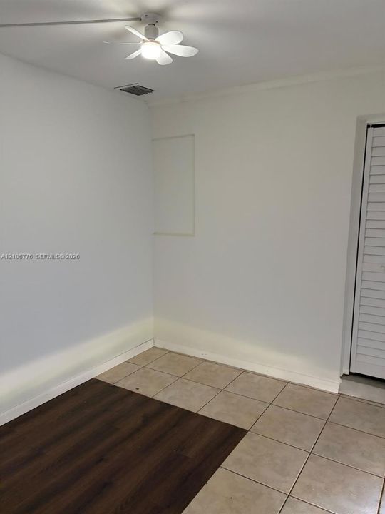 Room featuring a combination of tile and wood-finish flooring, a ceiling fan with integrated light, and a louvered bi-fold closet door