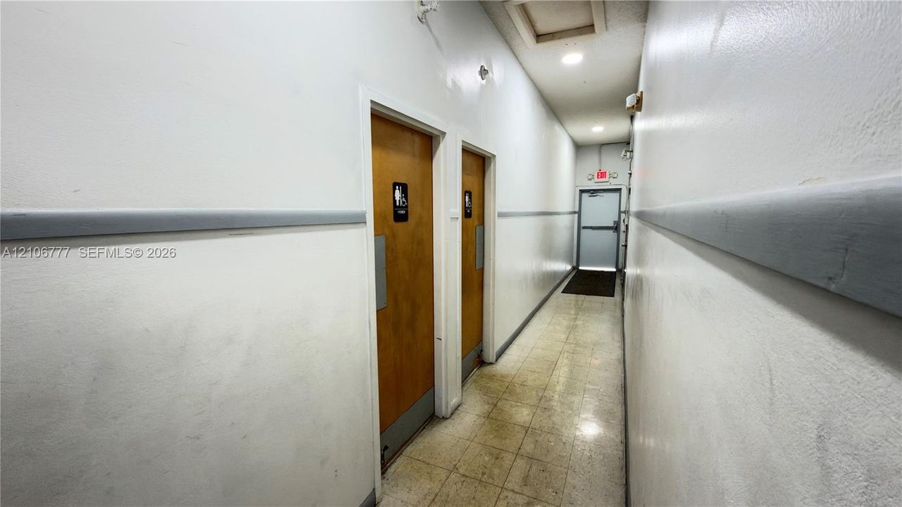 Hallway featuring recessed ceiling lighting, two wood-finish doors with metal push plates, and a metal-frame emergency exit door