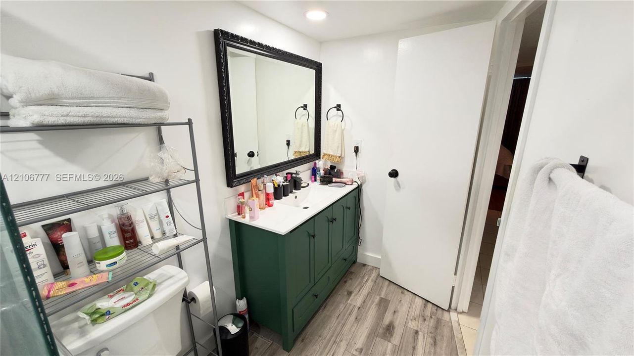 Bathroom vanity featuring a green cabinetry base, white countertop, integrated basin, and black-framed mirror, complemented by wood-finish flooring