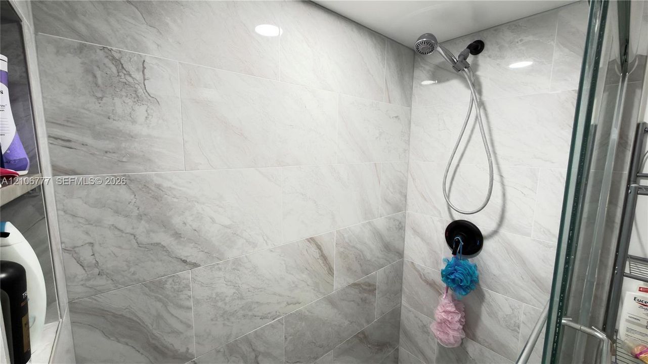 Walk-in shower featuring large-format stone-patterned wall tile, a handheld showerhead, matte black faucet trim, and a glass enclosure